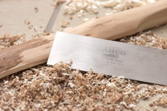 Eine Ziehklinge liegt neben feinen Spänen und einem Stück Holz