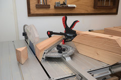 Auf dem Maschinentisch der CS 70 Tischkreissäge ist ein Holzbalken am Winkelanschlag festgezwingt, um eine Gehrung zu sägen